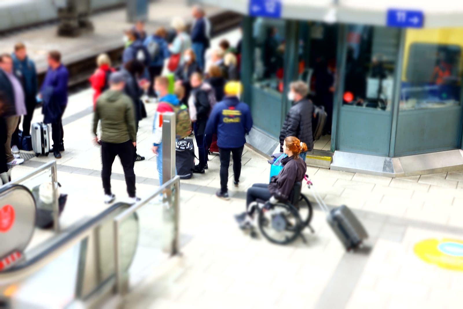 Reisende mit Gepäck in einer Bahnhofshalle.